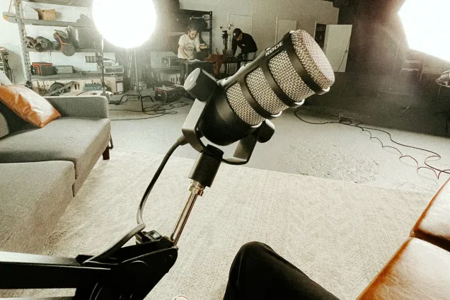9.jpg A photo of a microphone. Behind it a room with lights, sofas, and two people working at a desk.